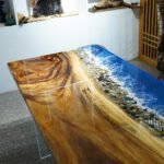 Side view of the Sylva Home custom ocean wave walnut epoxy dining table, model ET24, showcasing the table's edge and legs.